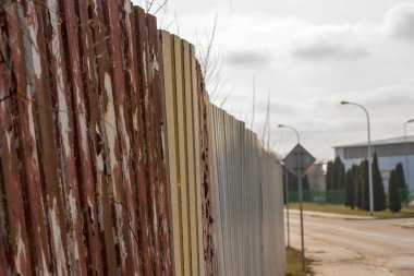 Bulutlu bir kış gününde endüstriyel bir bölgede ince (hafif paslı) çitler. Şubat ayının ilk saatlerinde bir üretim fabrikasını sanayi bölgesindeki bir sokaktan ayırmak..  