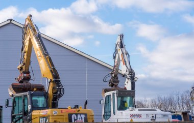 Construction of the new house.Poland Ostrowiec Swietokrzyski December 21, 2024 1:56 p. m. CAT and another excavator on the sky background. Construction machines standing on a fenced yard in front of a sheet metal hall.  clipart