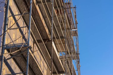 İnşaat alanının iskelesi. Termal modernizasyon sürecinden geçen bir apartman bloğunu (apartman binasını) çevreleyen inşaat iskelesi. İnşaat halindeki çok katlı bir bina, metalden yapılmış iskeleyle çevrili.. 