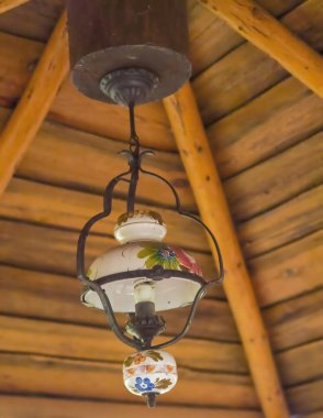 Evin tavanındaki lamba. Eski bir antika porselen elektrikli lamba (gaz lambasından yapılmıştır) ahşap bir çardakta tavanda asılı durur. Antika porselen elektrikli lamba, aslen bir gaz lambası, ahşap tavandan sarkıtılmış..  