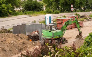 Polonya Ostrowiec Swietokrzyski 6 Haziran 2023: 53. MH 210 yeşil vintage kazıcı şehirdeki bir yol inşaatında. Yol inşaatında kullanılan MH 210 model yeşil bir kazıcı. Kum yığınları ve inşaat malzemelerinin arasına yerleştirilmiştir. . 