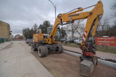 Polonya Ostrowiec Swietokrzyski 1 Şubat 2025 LiEBERR kazıcısı şehirdeki bir yol inşaatında. Sarı boya ve kırmızı çizgili ayrıntılara sahip makine büyük bir kova eklentisine sahip. Kısmen tamamlanmış bir yolda duruyor..