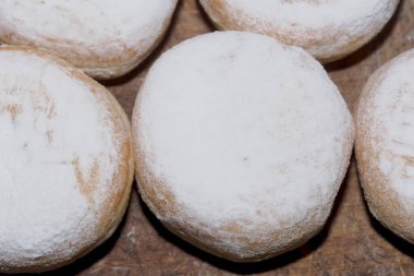 Yuvarlak çörekler üzerine pudra şekeri serpiştirilmiş ahşap tezgahın üzerinde duruyordu. Yuvarlak çörekler ahşap bir yüzey üzerinde duran kalın bir toz şekerle kaplıdır.. 