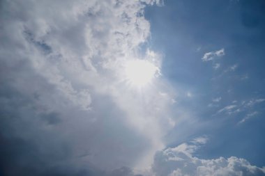 Kadife ve beyaz bulutlarla kaplı bahar gökyüzü ve yünlü su buharının içinde güneş şeffaf. Mavi gökyüzü beyaz ve gri bulutlarla dağılmış. Güneş kısmen gizlidir ve bulutların arasından yayılan parlak bir parıltı yayar. Bulutlar .