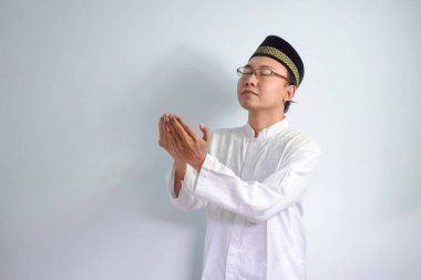 Gözlük takan Asyalı Müslüman adam ve beyaz bez Ramadhan ve Kurban Bayramı için dua eden el pozu veriyor. İzole edilmiş beyaz arkaplan
