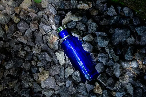 Çakıl ya da mercan zemin üzerinde koyu mavi parfüm şişesi