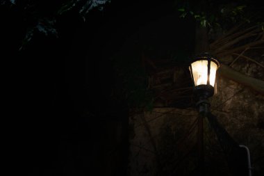 Ürkütücü karanlık bir gecede eski duvarda asılı klasik bir sokak feneri. Kopya alanı olan siyah sokak lambası