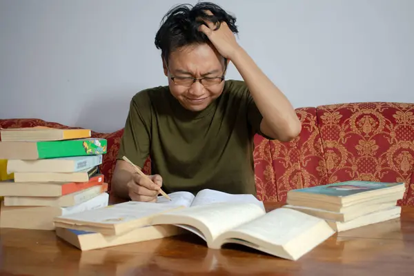 Asyalı genç erkek kitap okuyor. Sinirli bir jestle. Asyalı erkek, gözlüklü, kafası karışmış, beyaz arka planda.