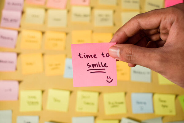Рука держит липкие заметки со словами Время улыбаться. Мотивационные слова для личного развития, вдохновляющий почерк. Загадочные ноты