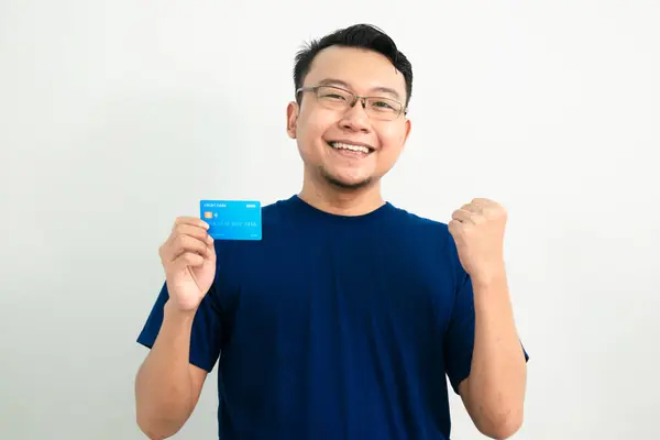 Mutlu Asyalı adam kredi kartıyla kutlama pozu veriyor. Bankacılık, finansal konsept ve el kaldırma hareketi. Mavi renk konsepti