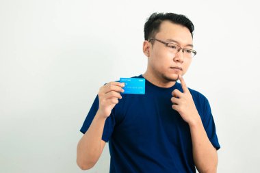Düşünceli Asyalı adam kredi kartını tutuyor. Bankacılık, finansal izole, mavi renk konsepti