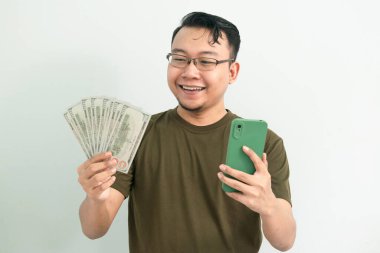 Mutlu Asyalı adam para ve telefonu elinde tutuyor. Bankacılık, finans ve teknoloji izole edilmiş, yeşil renk kavramı