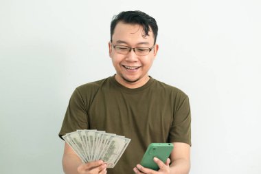 Mutlu Asyalı adam para ve telefonu elinde tutuyor. Bankacılık, finans ve teknoloji izole edilmiş, yeşil renk kavramı