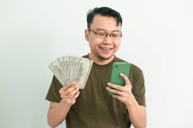Mutlu Asyalı adam para ve telefonu elinde tutuyor. Bankacılık, finans ve teknoloji izole edilmiş, yeşil renk kavramı