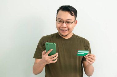 Mutlu Asyalı adamın kredi kartı ve telefonu var. Bankacılık, finans ve teknoloji izole edilmiş, yeşil renk kavramı