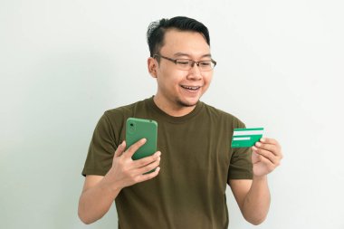 Mutlu Asyalı adamın kredi kartı ve telefonu var. Bankacılık, finans ve teknoloji izole edilmiş, yeşil renk kavramı