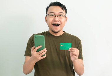 Mutlu Asyalı adamın kredi kartı ve telefonu var. Bankacılık, finans ve teknoloji izole edilmiş, yeşil renk kavramı