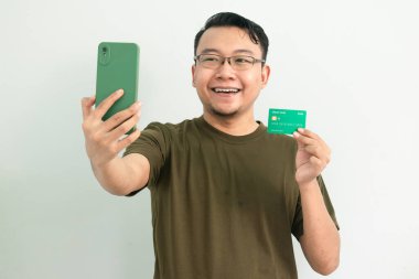 Mutlu Asyalı adamın kredi kartı ve telefonu var. Bankacılık, finans ve teknoloji izole edilmiş, yeşil renk kavramı