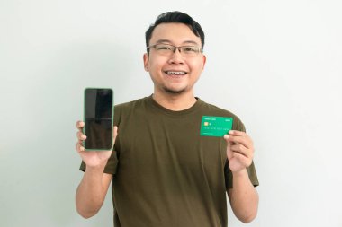 Mutlu Asyalı adamın kredi kartı ve telefonu var. Bankacılık, finans ve teknoloji izole edilmiş, yeşil renk kavramı