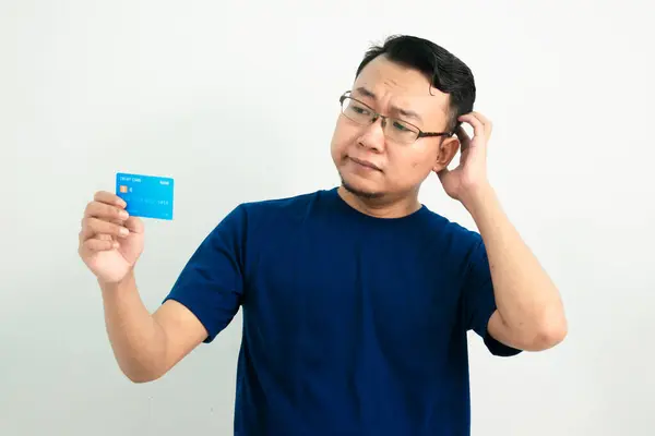 Düşünceli Asyalı adam kredi kartını tutuyor. Bankacılık, finansal izole, mavi renk konsepti