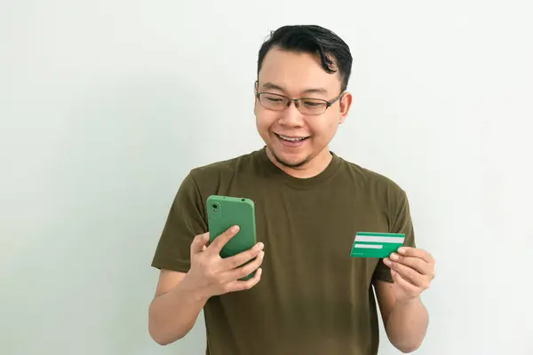 Mutlu Asyalı adamın kredi kartı ve telefonu var. Bankacılık, finans ve teknoloji izole edilmiş, yeşil renk kavramı
