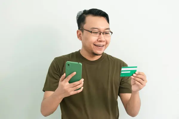 Mutlu Asyalı adamın kredi kartı ve telefonu var. Bankacılık, finans ve teknoloji izole edilmiş, yeşil renk kavramı