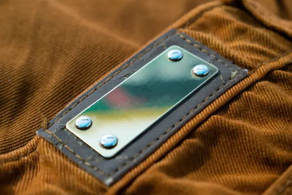 Parlak kahverengi kot pantolon, kumaş desen modeli üzerindeki boş metalik etiket.
