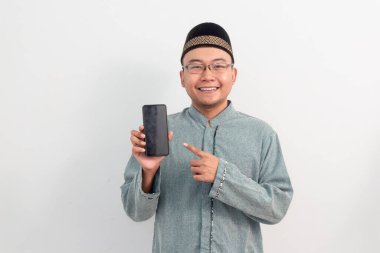 Beyaz elbiseli, gülümseyen Asyalı Müslüman adam telefon pozu, Ramazan Bayramı El Fitr ve Kurban Bayramı izole edilmiş beyaz arka planı kutluyor. İslami kutlama kavramı.