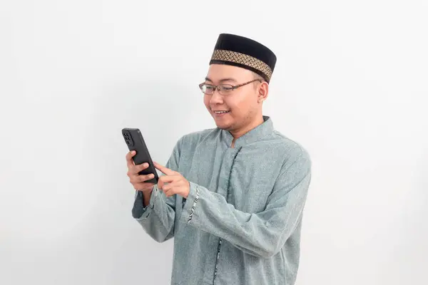 Elinde telefonla gülümseyen beyaz elbiseler giyen Asyalı Müslüman adam, Ramazan Bayramı ve Kurban Bayramı 'nda izole edilmiş beyaz arka planı kutluyor. İslami kutlama kavramı.