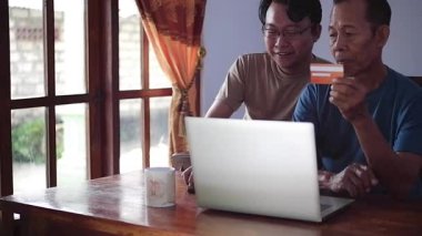 Mutlu yetişkin oğul ve yaşlı baba internet üzerinden ödeme yapıyorlar. Genç ve kıdemli birliktelik konsepti