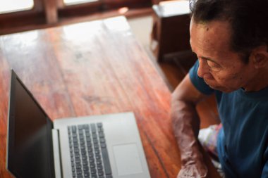 Oturma odasında dizüstü bilgisayar kullanan Asyalı yaşlı bir adam. Kıdemli ve teknoloji uzmanı.