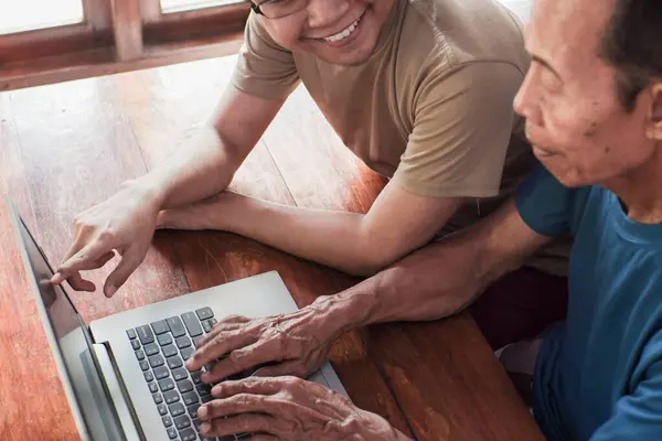 Mutlu yetişkin oğul yaşlı babaya dizüstü bilgisayar öğretiyor. Genç ve kıdemli birliktelik.
