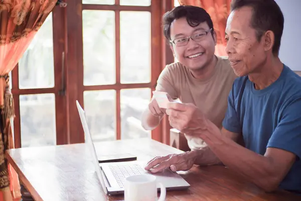 Mutlu yetişkin oğul ve yaşlı baba internet üzerinden ödeme yapıyorlar. Genç ve kıdemli birliktelik.