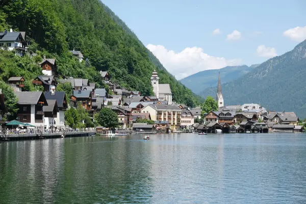 Görüntü, dağlarla göl arasında, sahil boyunca tekneleri ve binaları olan pitoresk bir Hallstatter kasabasını gösteriyor..