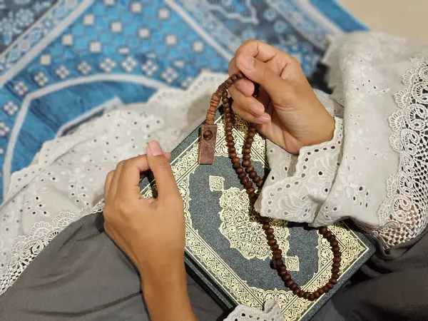 Genç bir Asyalı Müslüman kadın Ramazan ayında yerde tespih ve Kur 'an tutuyor.