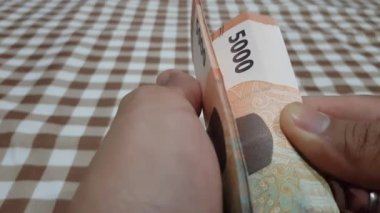 Beş bin rupia 'lık banknotları sayan bir adamın yakın çekimi. Nakit sayan bir iş adamı. Yatırım, para değişimi, rüşvet veya yolsuzluk kavramı.