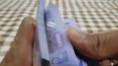 10 bin rupia 'lık banknotları sayan bir adamın yakın çekimi. Nakit sayan bir iş adamı. Yatırım, para değişimi, rüşvet veya yolsuzluk kavramı.