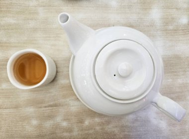 Çaydanlıklar hazır. Beyaz geleneksel seramik çaydanlık, sıcak çay fincanlarıyla eski, ahşap masa arka planında hazırlanıyor..