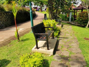 Banyumas, Endonezya - 11 Nisan 2024: bankı ve yolu olan bir park. Tezgah siyah ve beton döşemede.