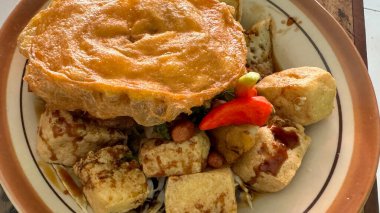 Tahu Kupat Endonezya, Surakarta 'dan geleneksel bir yemektir. Dilimlenmiş börek, sarı erişte, fasulye kabağı, kereviz ve kızarmış fıstıkla birlikte kızarmış tofu ve pirinç kekinden oluşuyor. Seramik tabakta kaplanmış, üzerinde de baharatlı fıstık var.