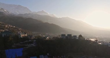 Sabahın erken saatlerinde, güneş doğarken Dharamshala şehrinin havadan görünüşü, şehirden karla kaplı dağlara yansıması, sisli ışıltı, 4k video