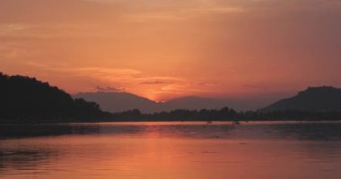 Dal Kashmir Gölü, Hindistan gün batımından sonra kırmızı görünüyor. Geçen tekneler suda bir yansıma yaratıyor. Günbatımı gökyüzünde bir renk yaratır ve bulutlar arka plandaki ışıkla aydınlatılır..
