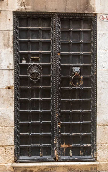 Image of a wooden door with decorative grid pattern. It has an oval shaped letterbox. Each door has a pull ring.. There is evidence of wear at the bottom of the door possible from being kicked open.