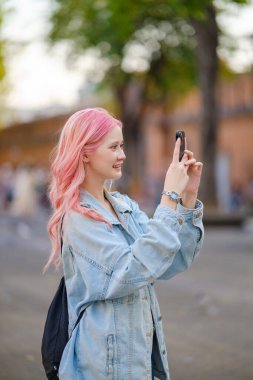 Uzun pembe saçlı genç bir kadın şehirde fotoğraf çekiyor. Yüksek kalite.