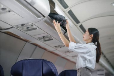 Asyalı bayan gezgin uçağa binerken bavullarını üstteki dolaba koyuyor. Yüksek kalite fotoğraf
