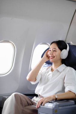 Uçakta oturan ve akıllı telefon kullanan Asyalı kadın uçak koltuğu pencere yolculuğu ve teknoloji konseptinin yanında müzik dinliyor. Yüksek kalite fotoğraf