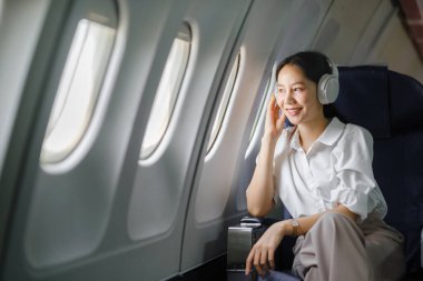 Uçakta oturan ve akıllı telefon kullanan Asyalı kadın uçak koltuğu pencere yolculuğu ve teknoloji konseptinin yanında müzik dinliyor. Yüksek kalite fotoğraf