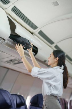 Asyalı bayan gezgin uçağa binerken bavullarını üstteki dolaba koyuyor. Yüksek kalite fotoğraf