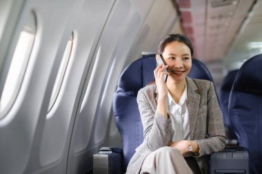 Genç Asyalı kadın uçakta oturuyor ve akıllı telefonla konuşuyor. Genç bayan gezgin cep telefonuyla konuşuyor. Yüksek kalite fotoğraf