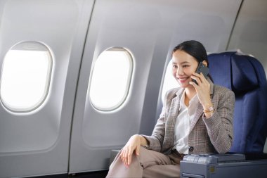 Genç Asyalı kadın uçakta oturuyor ve akıllı telefonla konuşuyor. Genç bayan gezgin cep telefonuyla konuşuyor. Yüksek kalite fotoğraf